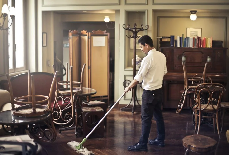 A person in a protective suit sanitizing a wooden shelf in a modern home environment.